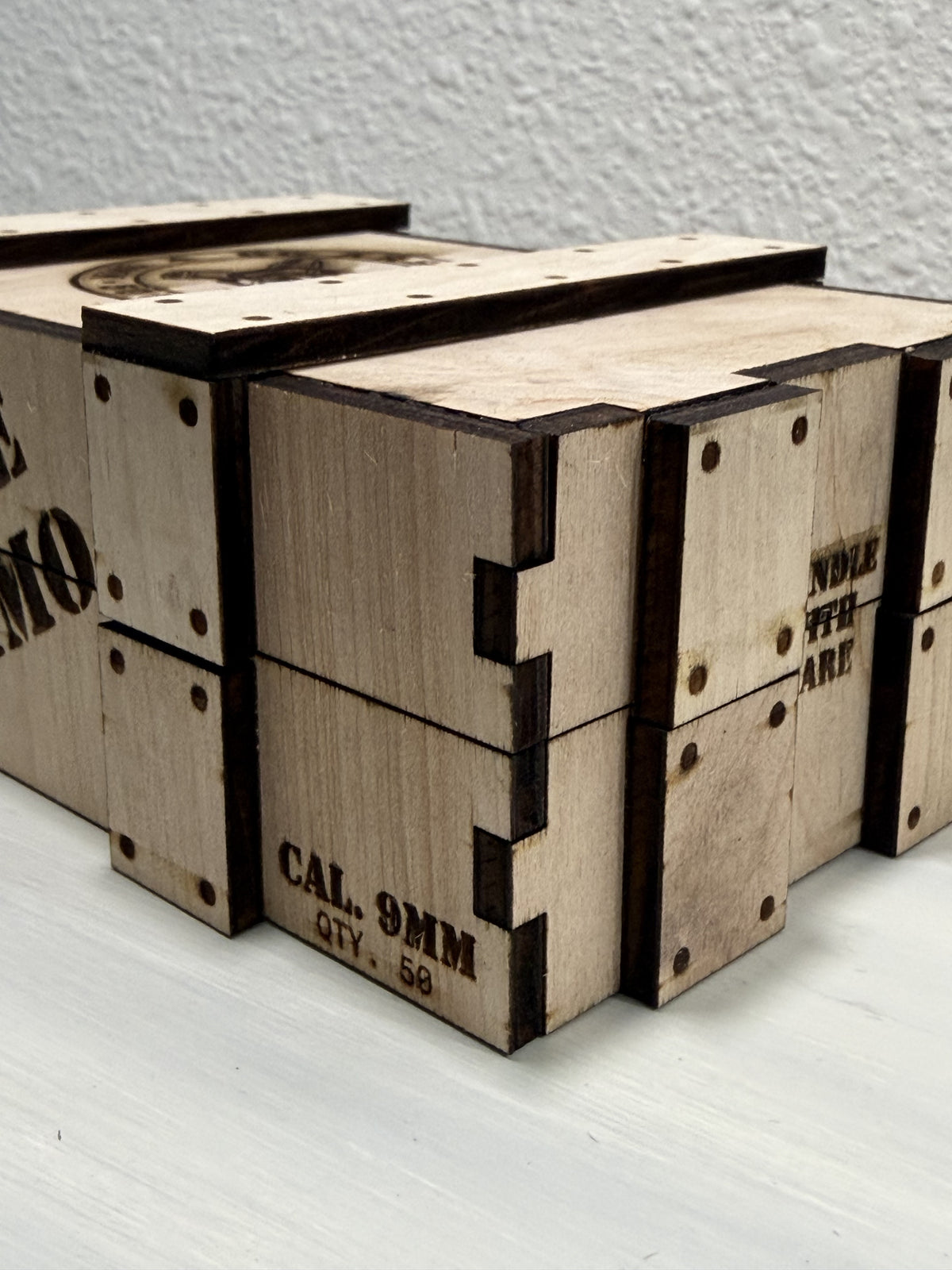 Close view of finger-jointed plywood corners, layered reinforcement straps and engraved faux fasteners.