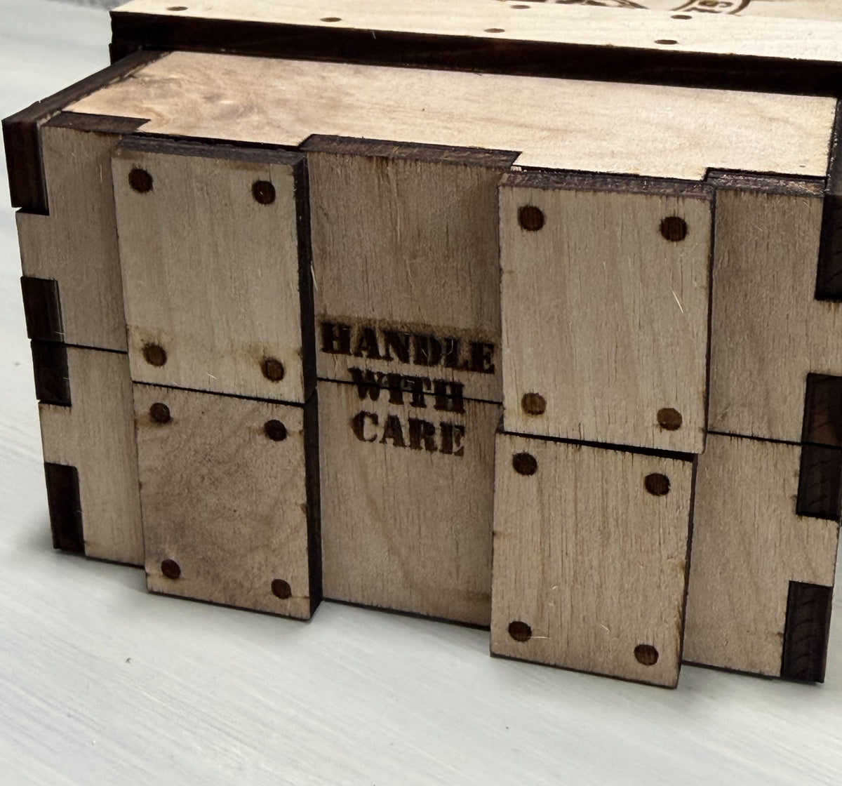 Wooden crate end engraved HANDLE WITH CARE with layered wooden straps.